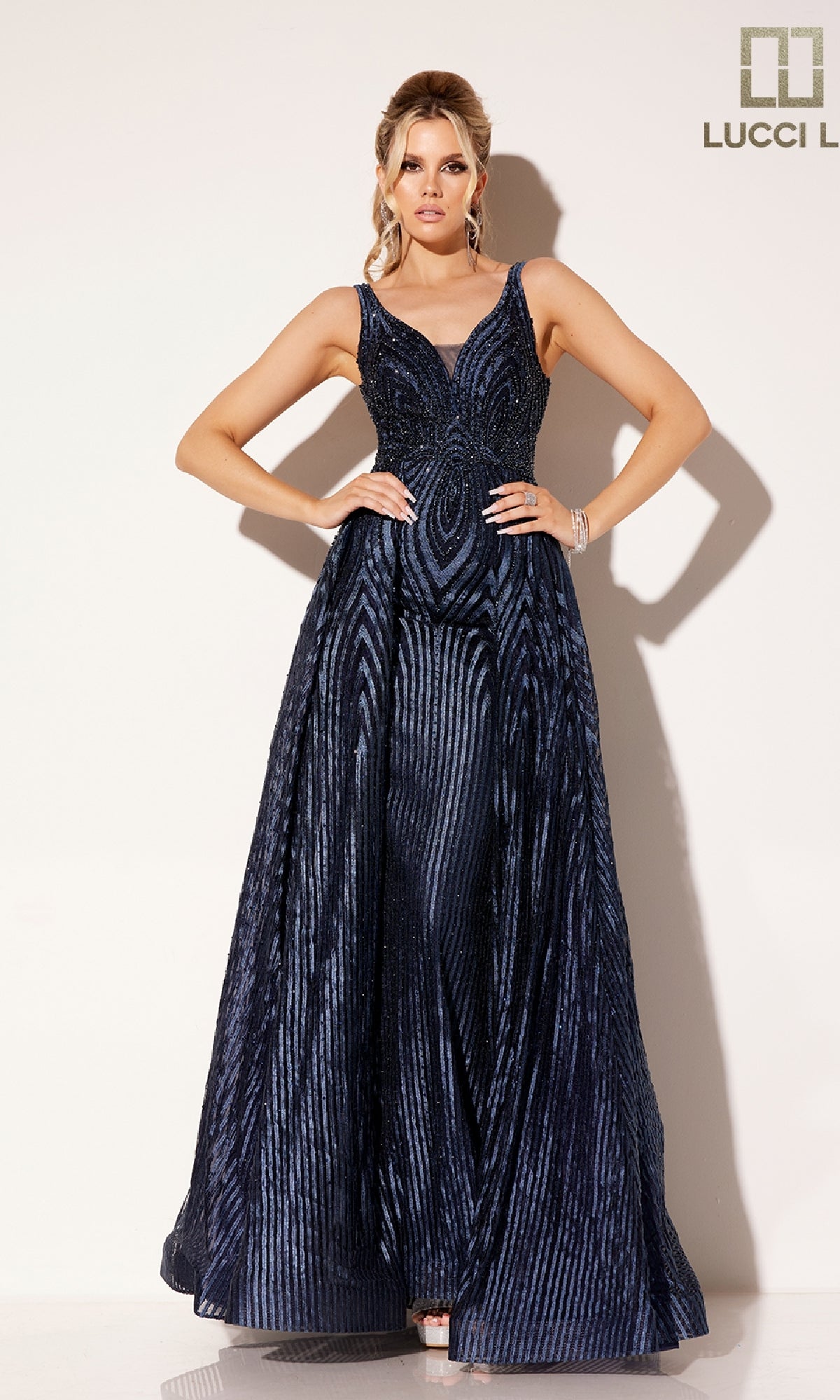 A woman poses against a plain light background wearing the Lucci Lu C8074 long prom dress, a sleeveless navy blue gown with a geometric striped pattern.